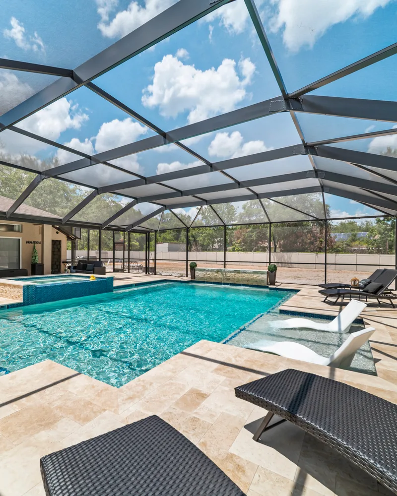 Custom pool with a stacked stone water wall and ivory travertine decking built by Pool Perfection in Odessa