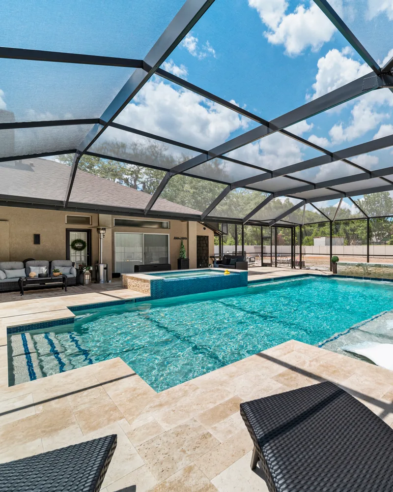 Custom pool with a stacked stone water wall and ivory travertine decking built by Pool Perfection in Odessa