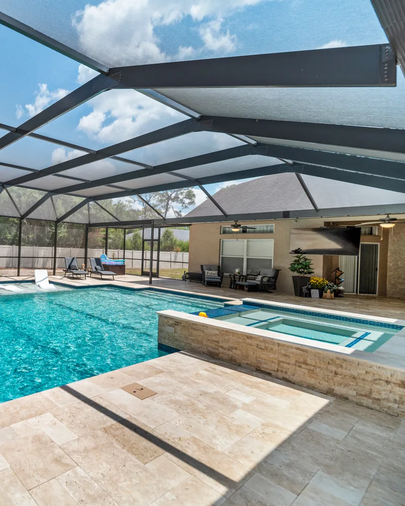 Custom pool with a stacked stone water wall and ivory travertine decking built by Pool Perfection in Odessa