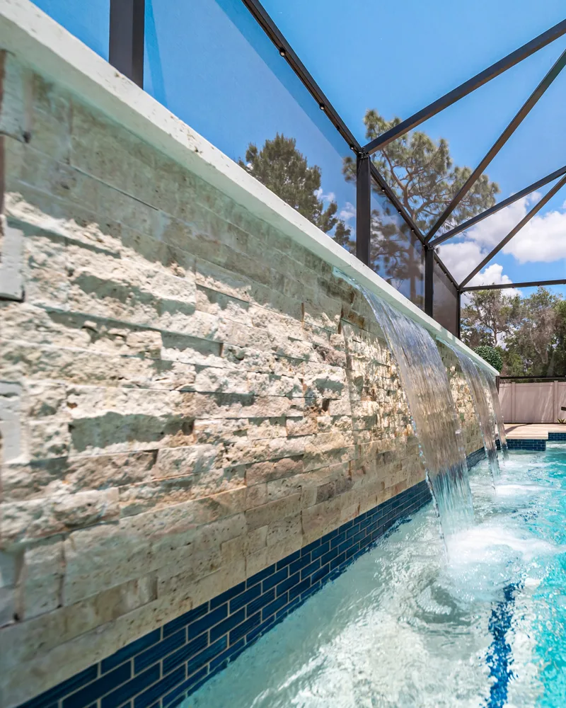 Custom pool with a stacked stone water wall and ivory travertine decking built by Pool Perfection in Odessa
