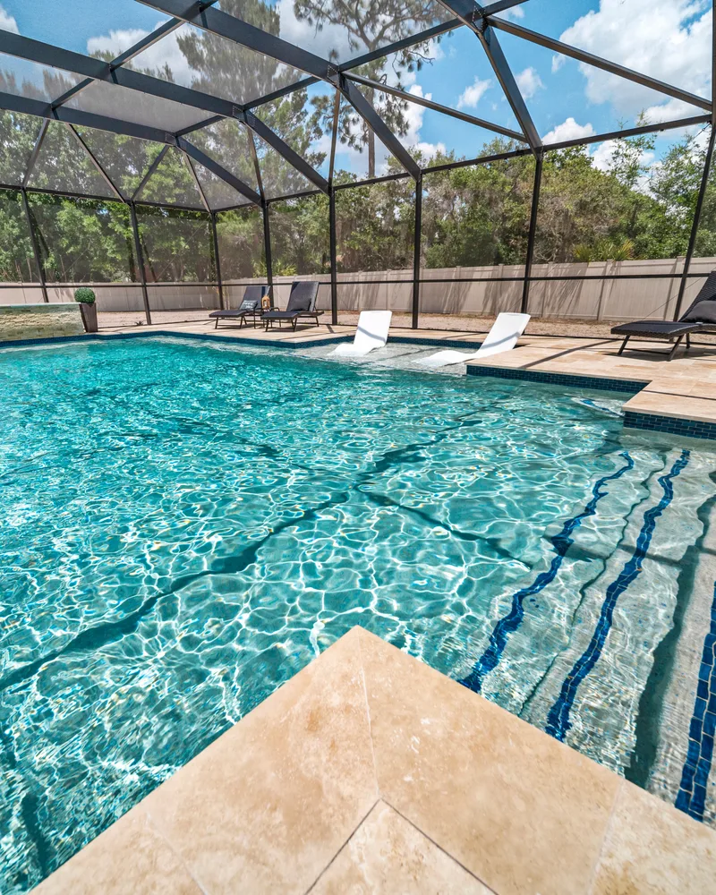 Custom pool with a stacked stone water wall and ivory travertine decking built by Pool Perfection in Odessa