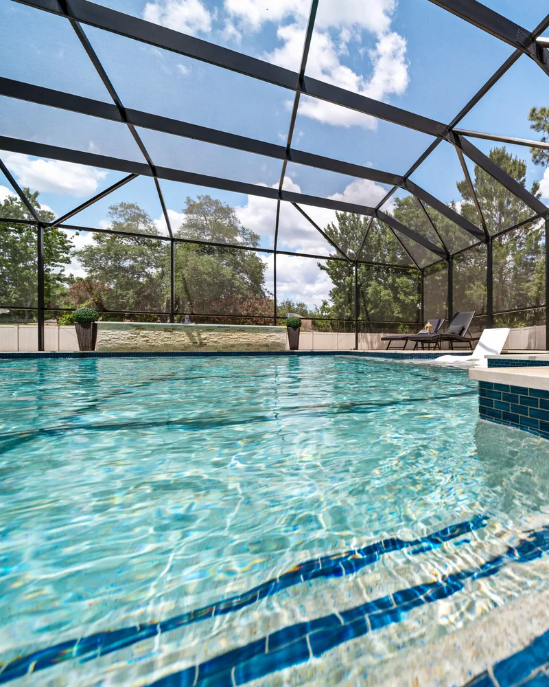 Custom pool with a stacked stone water wall and ivory travertine decking built by Pool Perfection in Odessa