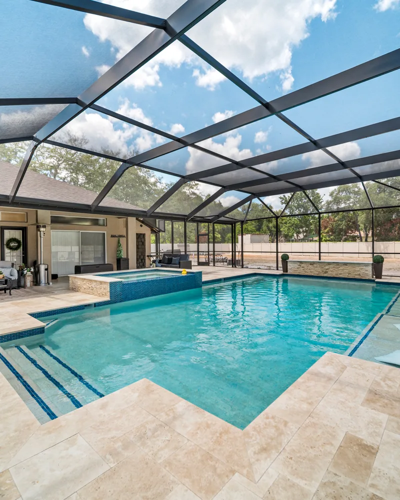 Custom pool with a stacked stone water wall and ivory travertine decking built by Pool Perfection in Odessa