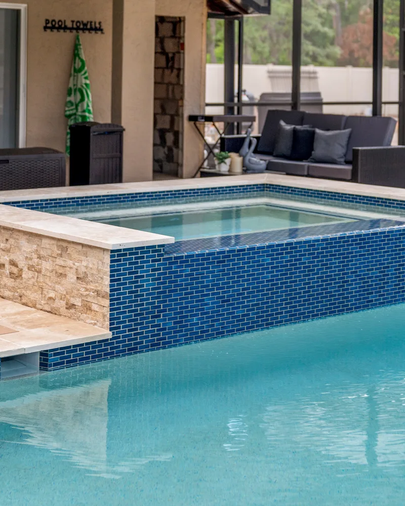 Custom pool with a stacked stone water wall and ivory travertine decking built by Pool Perfection in Odessa