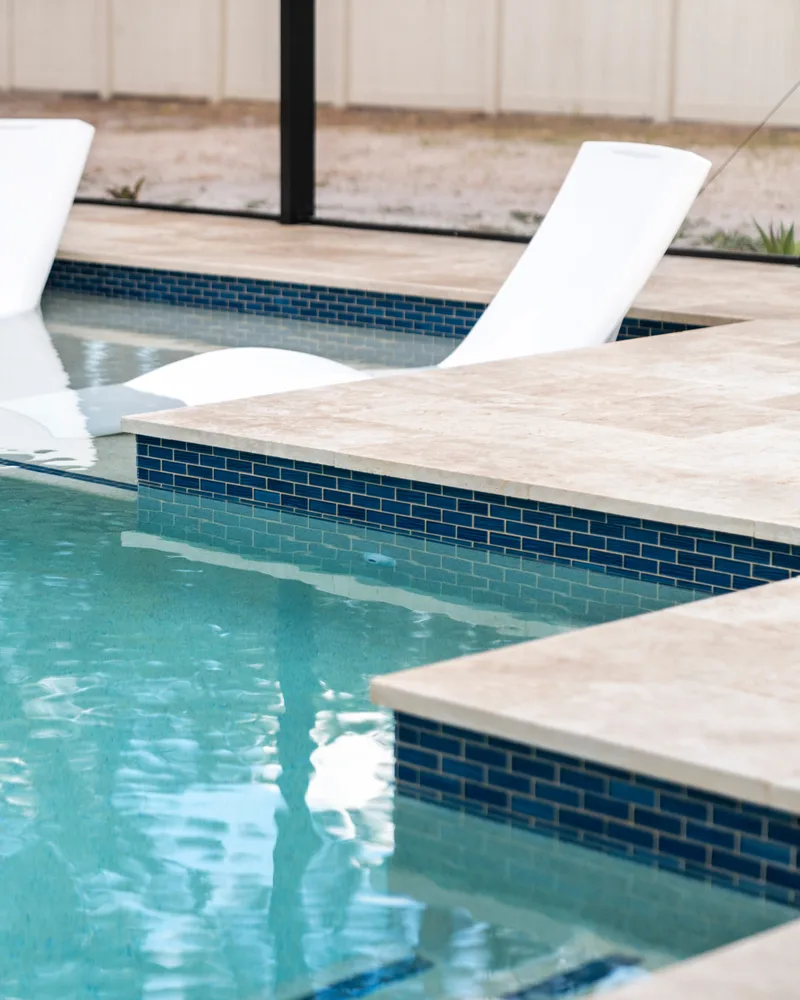 Custom pool with a stacked stone water wall and ivory travertine decking built by Pool Perfection in Odessa
