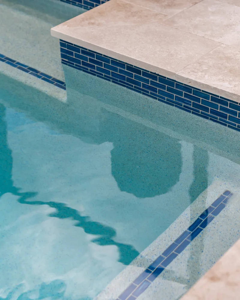 Custom pool with a stacked stone water wall and ivory travertine decking built by Pool Perfection in Odessa