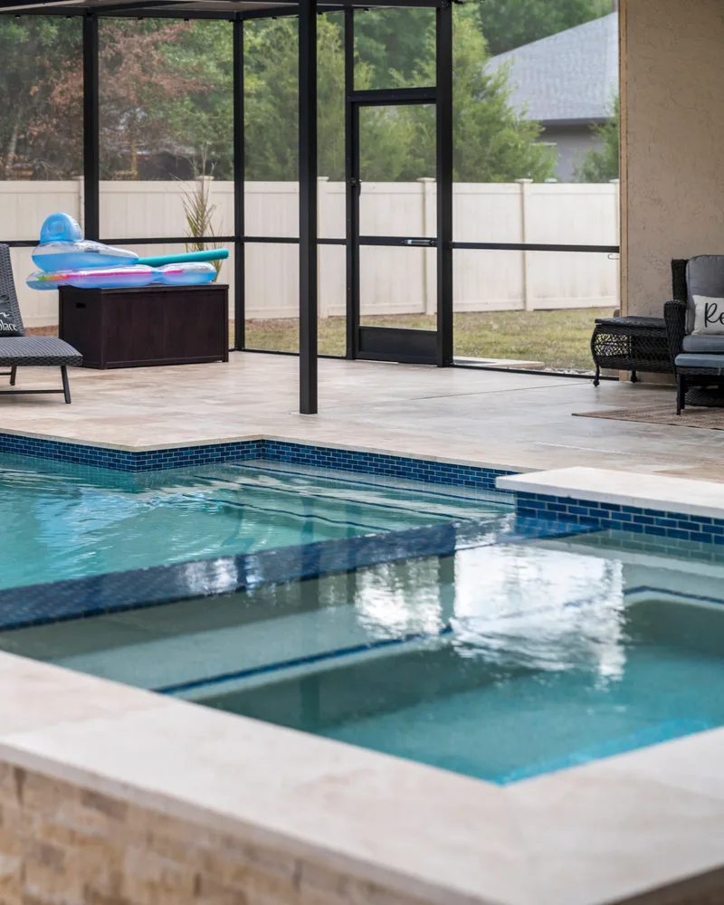 Custom pool with a stacked stone water wall and ivory travertine decking built by Pool Perfection in Odessa