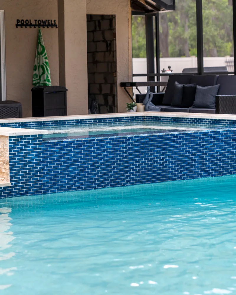 Custom pool with a stacked stone water wall and ivory travertine decking built by Pool Perfection in Odessa