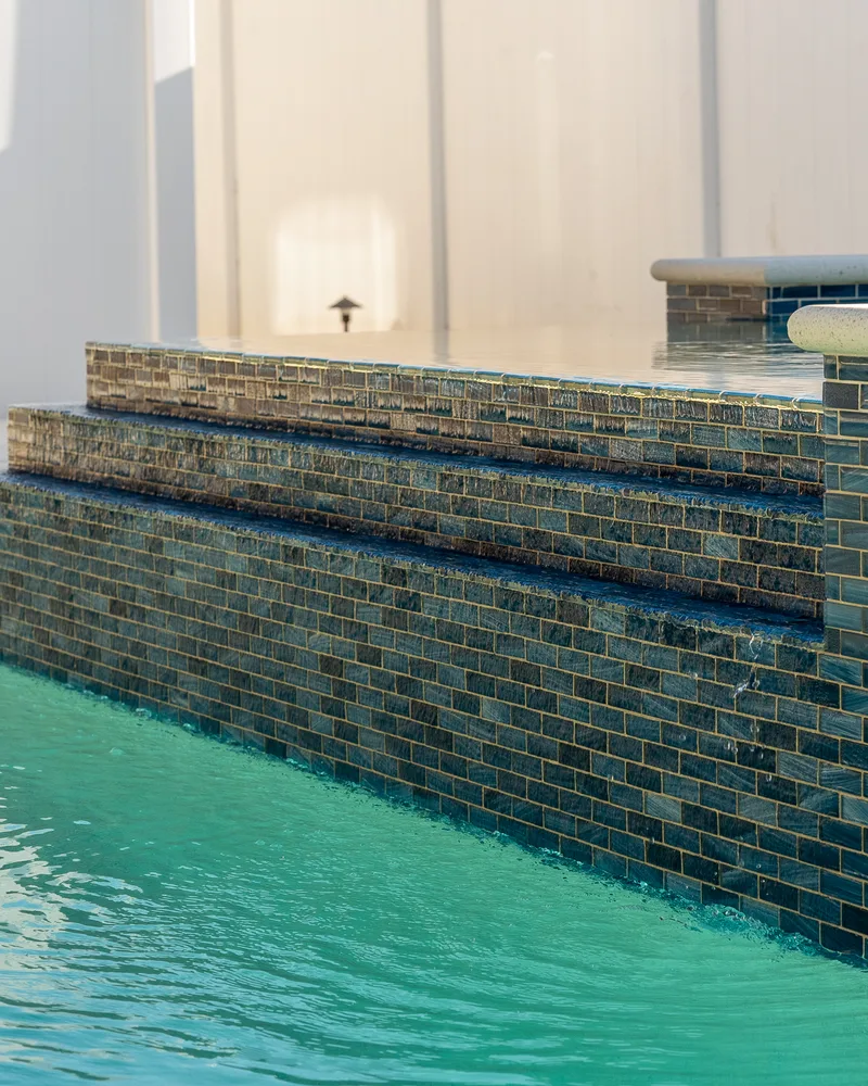 Water cascading from a raised spa wall into a light blue pool