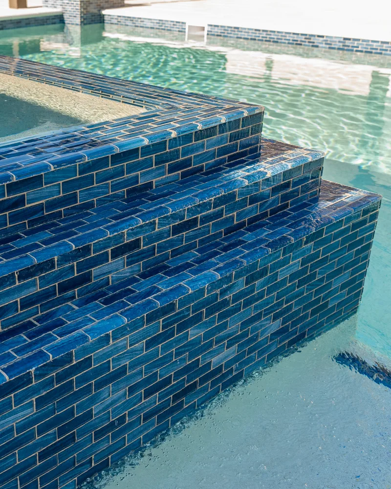 Custom pool with a water cascade and navy waterline tile built by Pool Perfection in Seminole