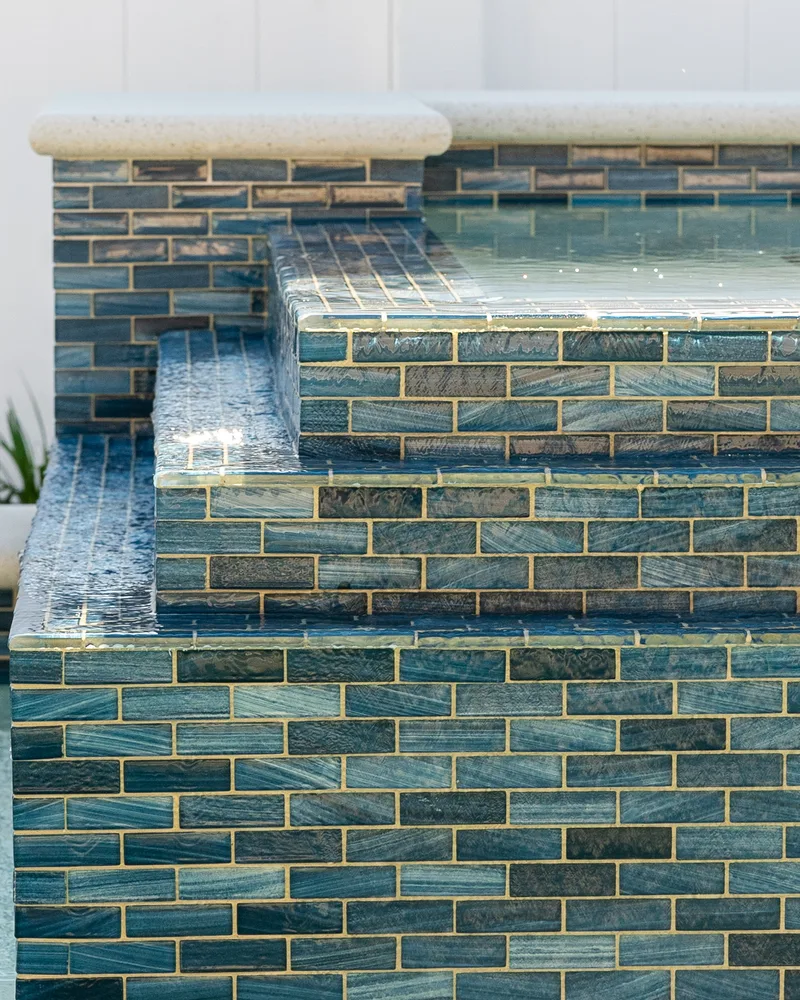 Custom pool with a water cascade and navy waterline tile built by Pool Perfection in Seminole
