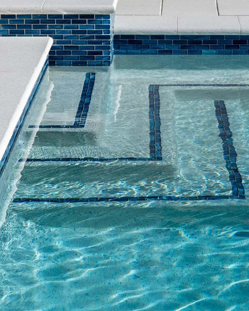 Custom pool with a water cascade and navy waterline tile built by Pool Perfection in Seminole