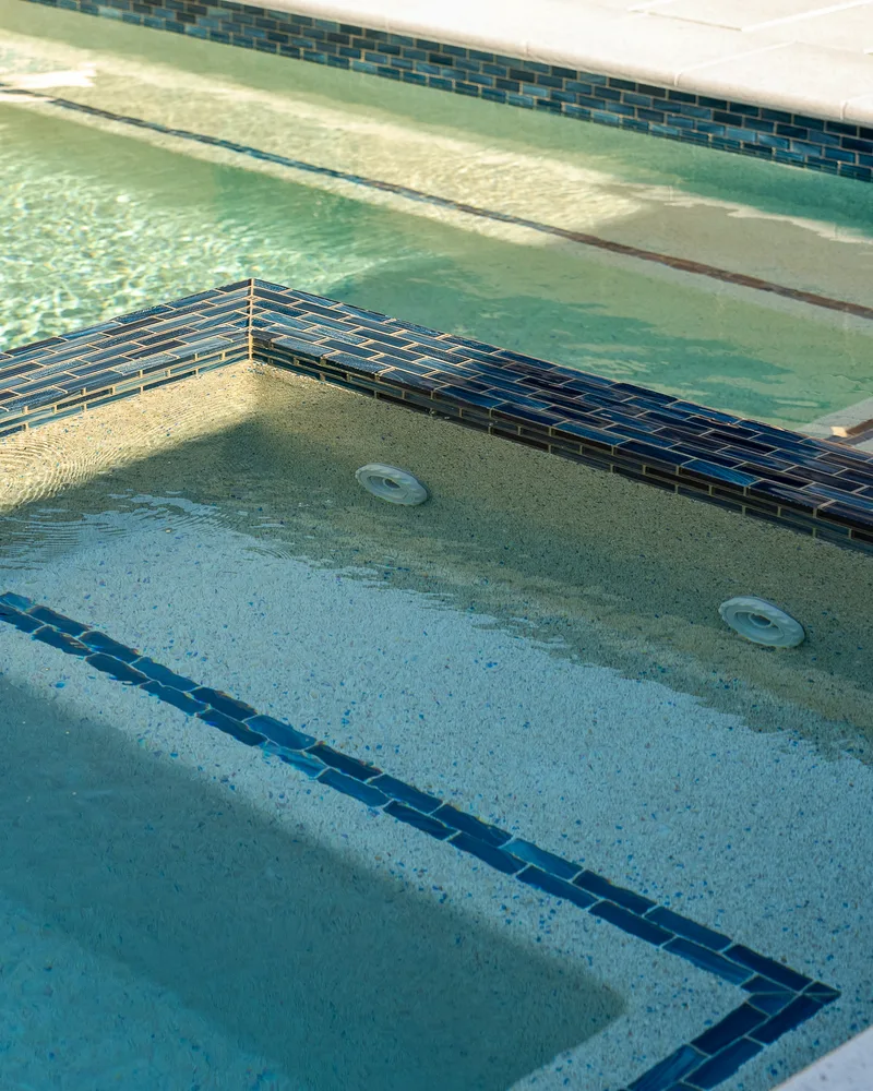 Custom pool with a water cascade and navy waterline tile built by Pool Perfection in Seminole