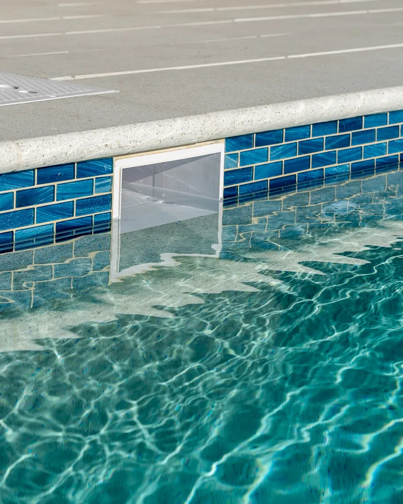Close view of deep navy glass waterline tile against pale blue pool water