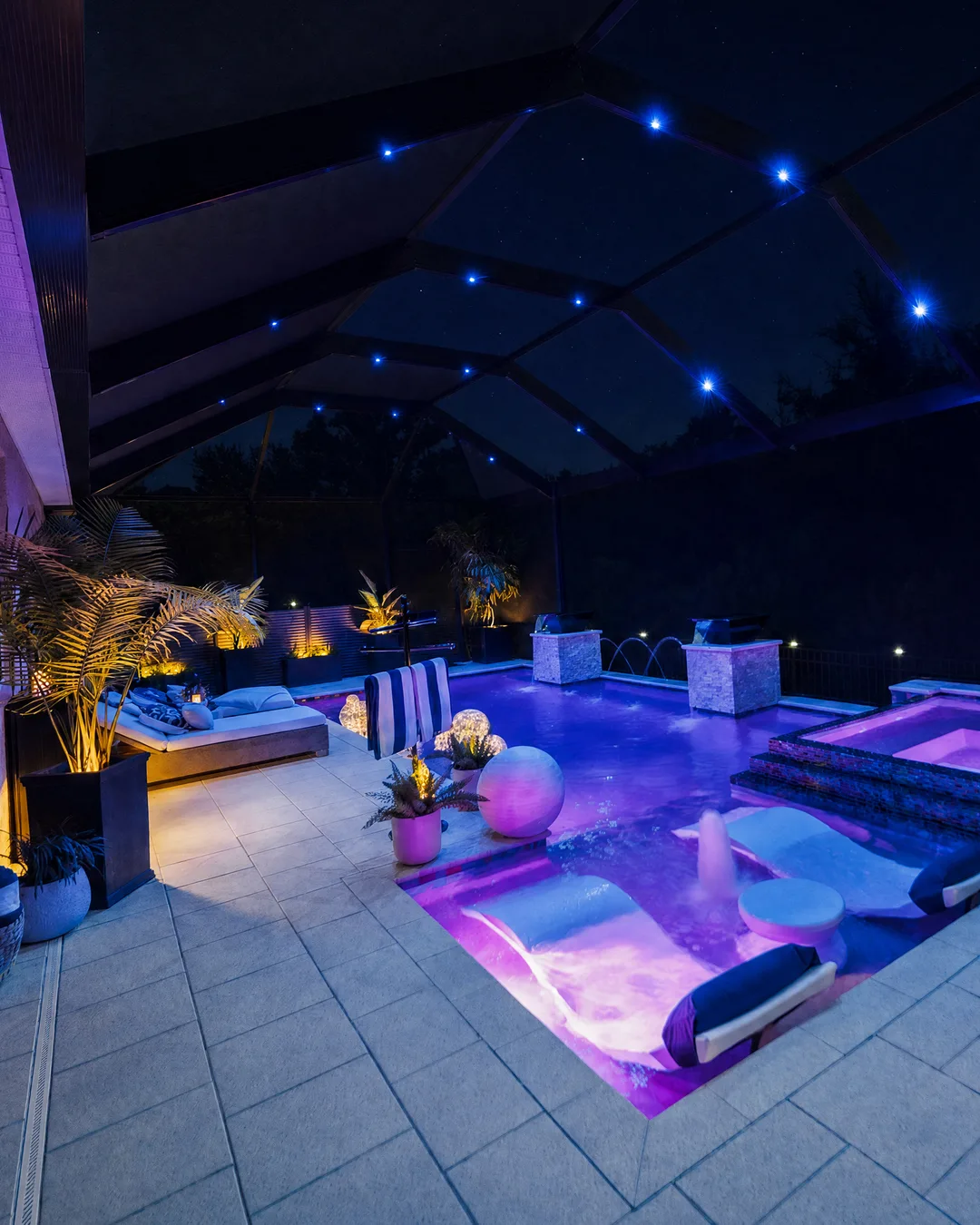 Tampa custom pool and spa lit deep blue at night, with a tanning ledge, loungers and an uplit screen enclosure