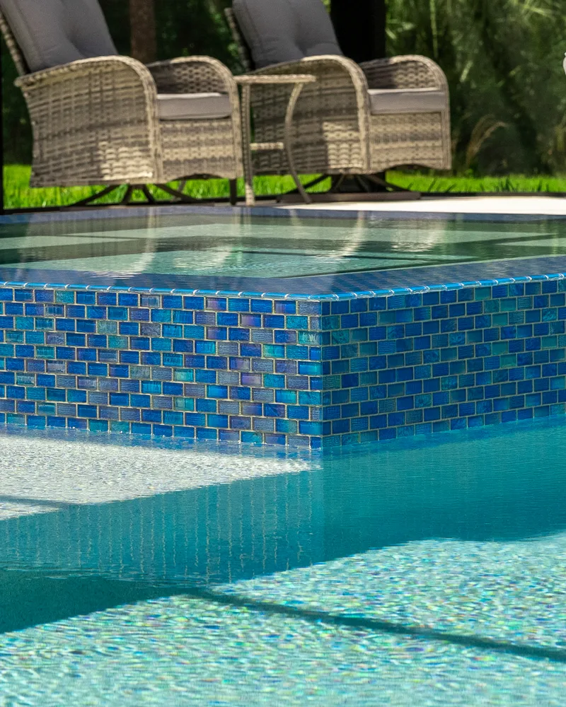 Raised spa clad in blue glass mosaic tile spilling into the pool below